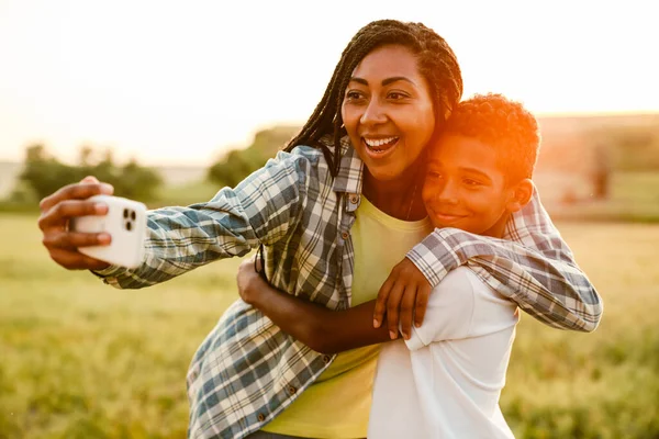 Siyah anne piknik sırasında oğluyla cep telefonunda fotoğraf çekiyor.