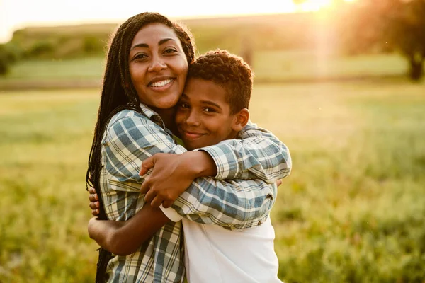Black mother hugging her son and smiling on summer field