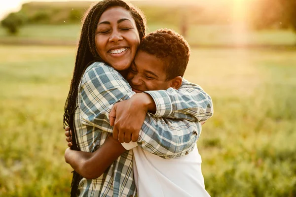 Siyah anne oğlunu kucaklıyor ve yaz tarlasında gülümsüyor.