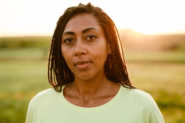 At kuyruklu siyahi kadın, dışarıda dikilirken kameraya bakıyor ve poz veriyor.