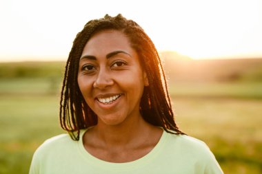 At kuyruklu siyahi bir kadın dışarıda kameraya bakıp gülümsüyor.