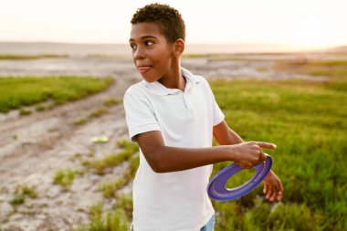 Beyaz tişörtlü siyah çocuk dışarıda frizbiyle oynuyor.