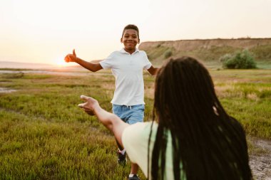 Siyah anne, piknik sırasında gülümseyen oğluna elini uzatıyor.