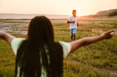 Siyah anne, piknik sırasında gülümseyen oğluna elini uzatıyor.