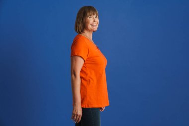 Son sınıf öğrencisi kadın tişört giyiyor gülümsüyor ve mavi duvardan dışarı bakıyor.