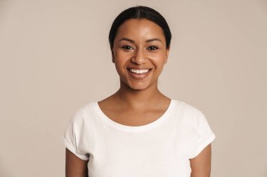 Tişört giyen genç siyah kadın gülümsüyor ve beyaz duvarın üzerinden izole edilmiş kameraya bakıyor.