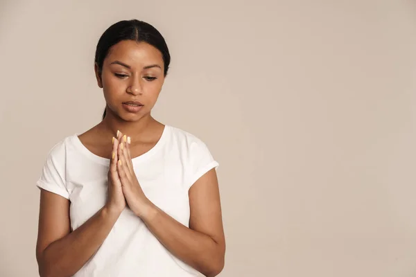 年轻的黑人妇女穿着T恤衫摆着姿势 在白墙外做着孤立的祷告动作 — 图库照片
