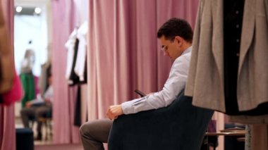 Gözlüklü, konsantreli bir adam elbise mağazasında soyunma odasında bekliyor.