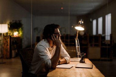 Ofiste çalışırken gözlüklü, cep telefonuyla konuşan beyaz sakallı adam.