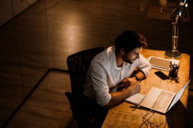 Akşamları ofiste dizüstü bilgisayarla çalışan beyaz sakallı adam.