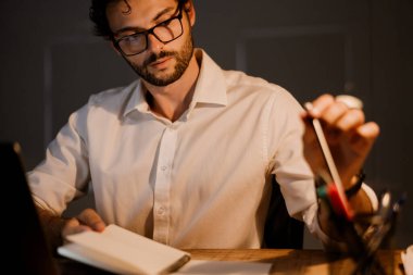 Beyaz sakallı adam ofiste çalışırken ajandasına notlar yazıyor.