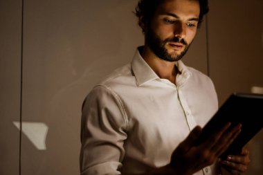 Akşam ofiste tablet bilgisayarla çalışan beyaz sakallı adam.