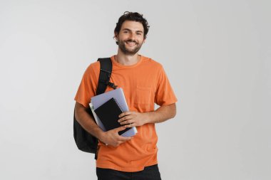 Sırt çantasıyla poz verirken gülümseyen genç adam ve beyaz arka planda izole edilmiş egzersiz kitapları.