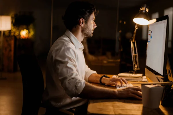 屋内のオフィスで夜にコンピュータと仕事をする白い髭の男 — ストック写真