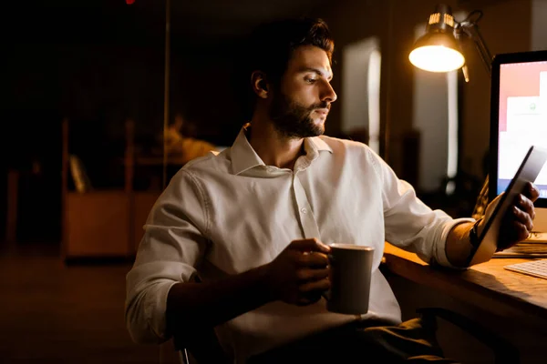 オフィスでタブレットPcと仕事をしながら白い髭の男がコーヒーを飲む — ストック写真