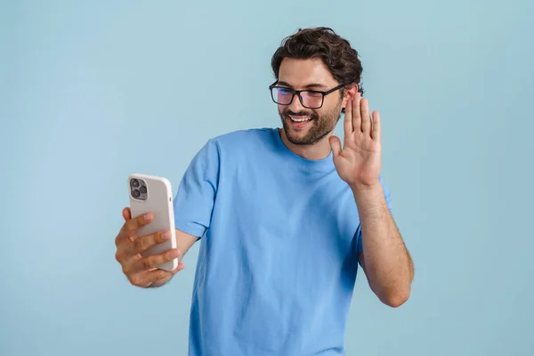 Young Brunette Man Gesturing While Using Mobile Phone Isolated Blue — Zdjęcie stockowe
