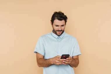 Beyaz tüylü adam sürpriz yapıyor ve bej arka planda izole edilmiş cep telefonu kullanıyor.