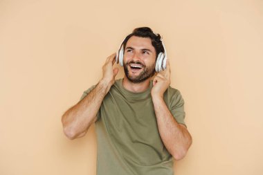 Beyaz kıllı adam gülüyor. Bej arka planda izole edilmiş kulaklıklarla müzik dinliyor.