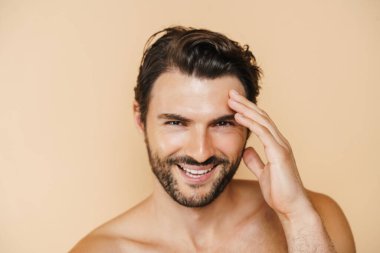 Yüzü bej rengi arka planda soyutlanırken yarı çıplak bir adam gülüyor.