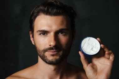 Siyah arka planda izole edilmiş yüz kremi gösterirken yarı çıplak bir adam poz veriyor.