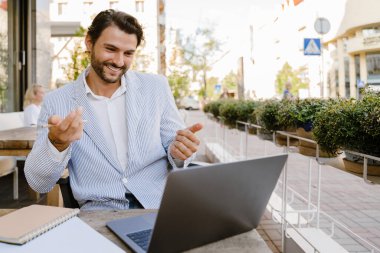 Genç adam dışarıda kafede otururken dizüstü bilgisayarla çalışıyor.