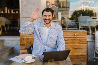 Genç adam dışarıda kafede otururken dizüstü bilgisayarla çalışıyor.