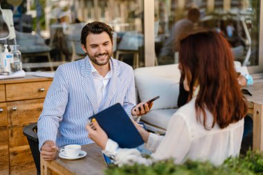 Genç bir adam ve kadın açık kafede iş görüşmesinde birlikte çalışıyorlar.