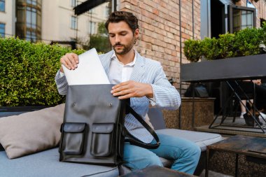 Genç adam dışarıda kafede otururken dizüstü bilgisayarla çalışıyor.