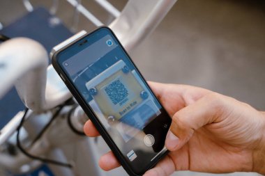 Beyaz adam dışarıda bisiklet kiralamak için QR kodunu cep telefonuyla tarıyor.
