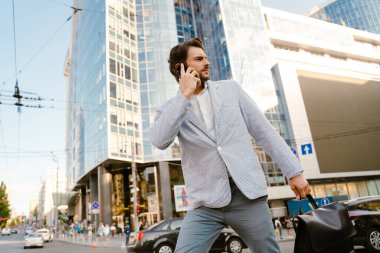 Ceketli genç adam şehir caddesinde yürürken cep telefonuyla konuşuyor.