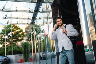 Dışarıda cep telefonuyla konuşurken gülümseyen ceketli genç adam.