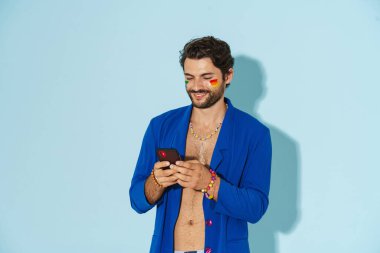 Mavi ceketli genç adam gülüyor ve mavi arka planda cep telefonu kullanıyor.