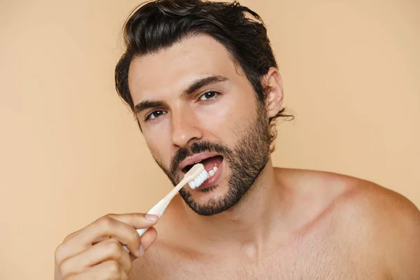 年轻的半裸男子在刷牙的时候看着相机 在米色的背景下被隔离了 — 图库照片