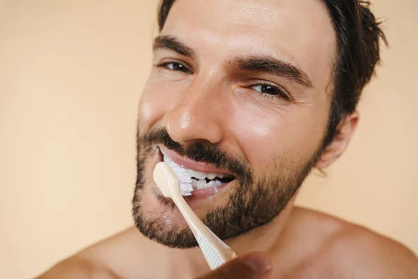 年轻的半裸男子笑着刷牙时被米色背景隔离了 — 图库照片