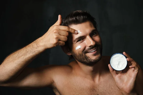 Joven Hombre Semidesnudo Sonriendo Mientras Aplica Crema Facial Aislada Sobre —  Fotos de Stock