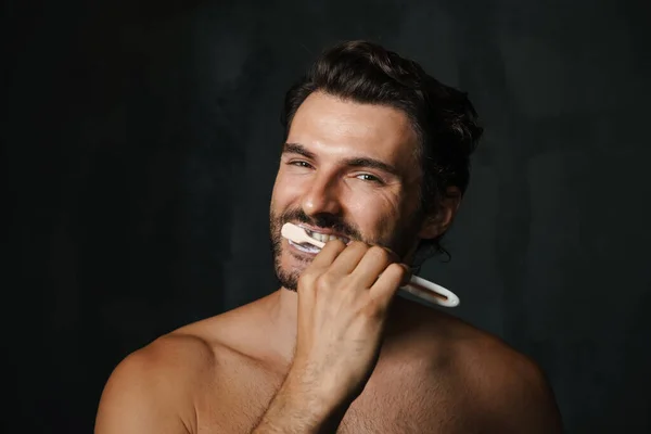 年轻的半裸男子笑着刷牙时被黑色背景隔开了 — 图库照片