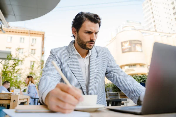 Young Man Wearing Jacket Writing Notes While Working Laptop Cafe — Stockfoto