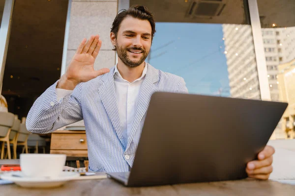 Genç adam dışarıda kafede otururken dizüstü bilgisayarla çalışıyor.