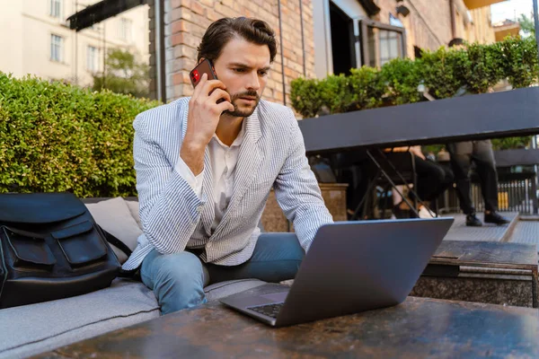 Young Man Talking Mobile Phone While Working Laptop Cafe Outdoors — Stockfoto