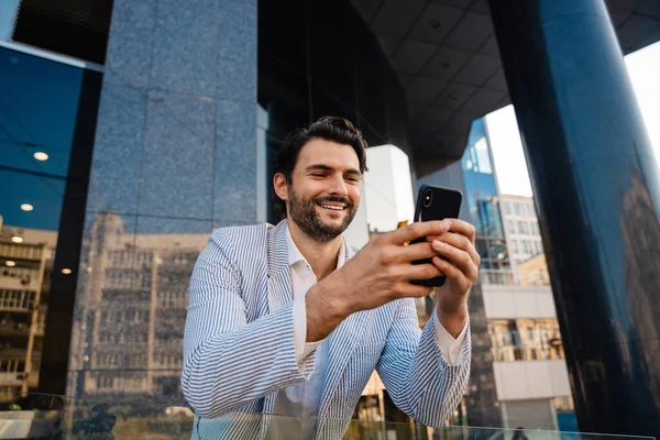 Young man wearing jacket smiling and using mobile phone outdoors