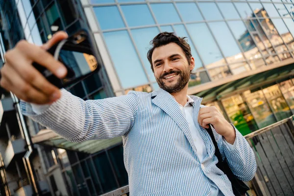 Genç adam dışarıda cep telefonunda fotoğraf çekerken gülümsüyor.