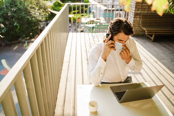 Young Man Face Mask Talking Cellphone While Working Laptop Cafe — Stockfoto