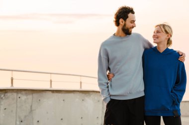 Genç bir adam ve bir kadın dışarıda birlikte spor yaparken sarılıyorlar.