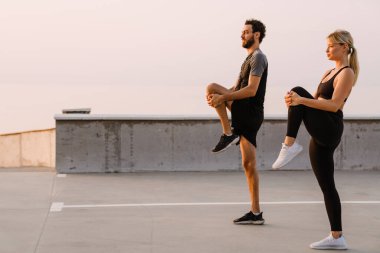 Genç adam ve kadın dışarıda park alanında çalışırken egzersiz yapıyorlar.