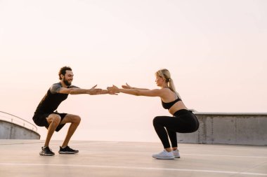 Genç adam ve kadın dışarıda park alanında çalışırken egzersiz yapıyorlar.