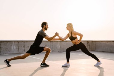 Genç adam ve kadın dışarıda park alanında çalışırken egzersiz yapıyorlar.