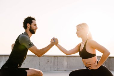 Genç adam ve kadın dışarıda park alanında çalışırken egzersiz yapıyorlar.