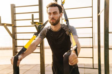 Genişletici bantlarla spor yapan genç bir adam açık havada spor yapıyor.