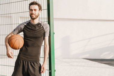 Genç beyaz adam dışarıda spor alanında topla çalışıyor.
