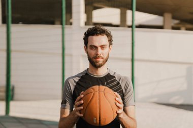 Genç beyaz adam dışarıda spor alanında topla çalışıyor.